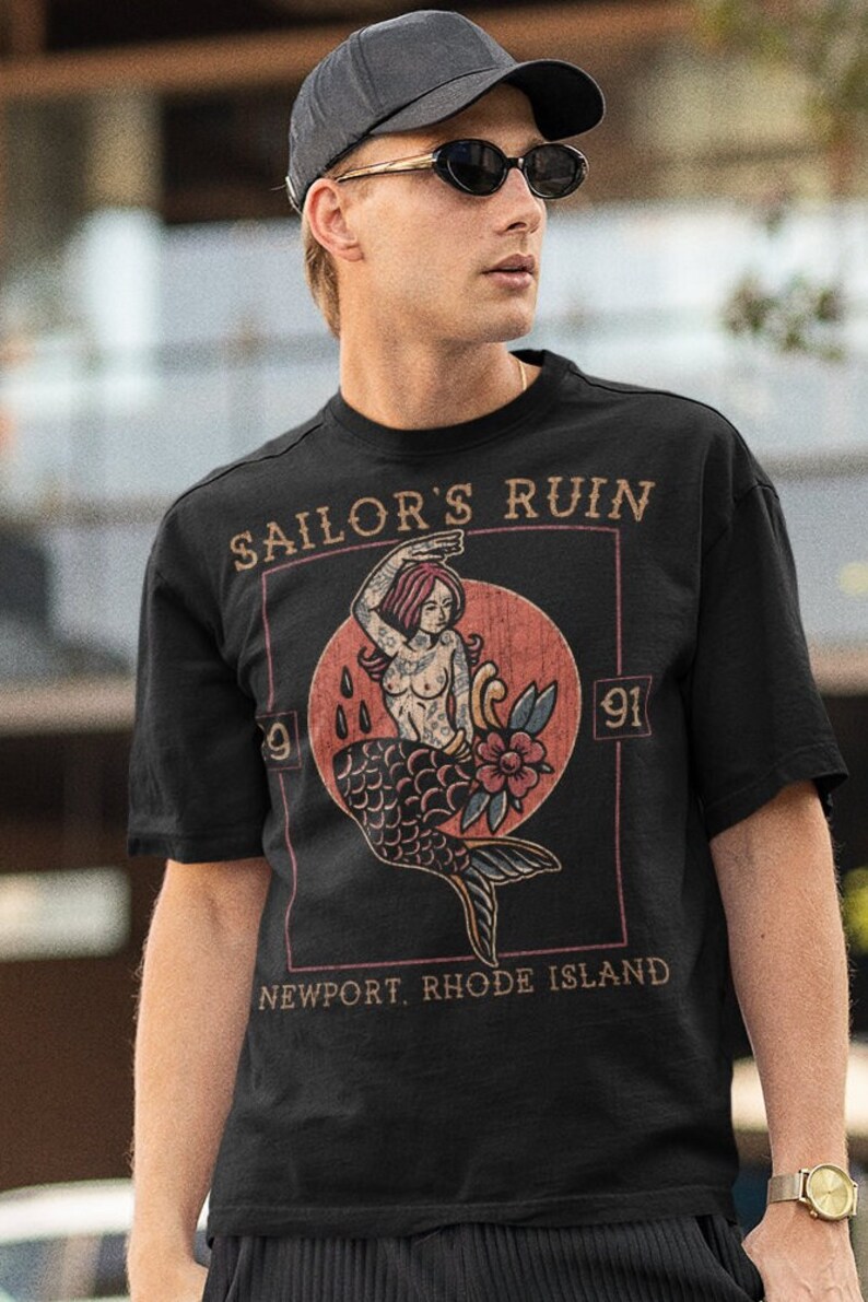 May include: A black t-shirt with a vintage-style graphic of a mermaid with the text "Sailor's Ruin" and "Newport, Rhode Island".