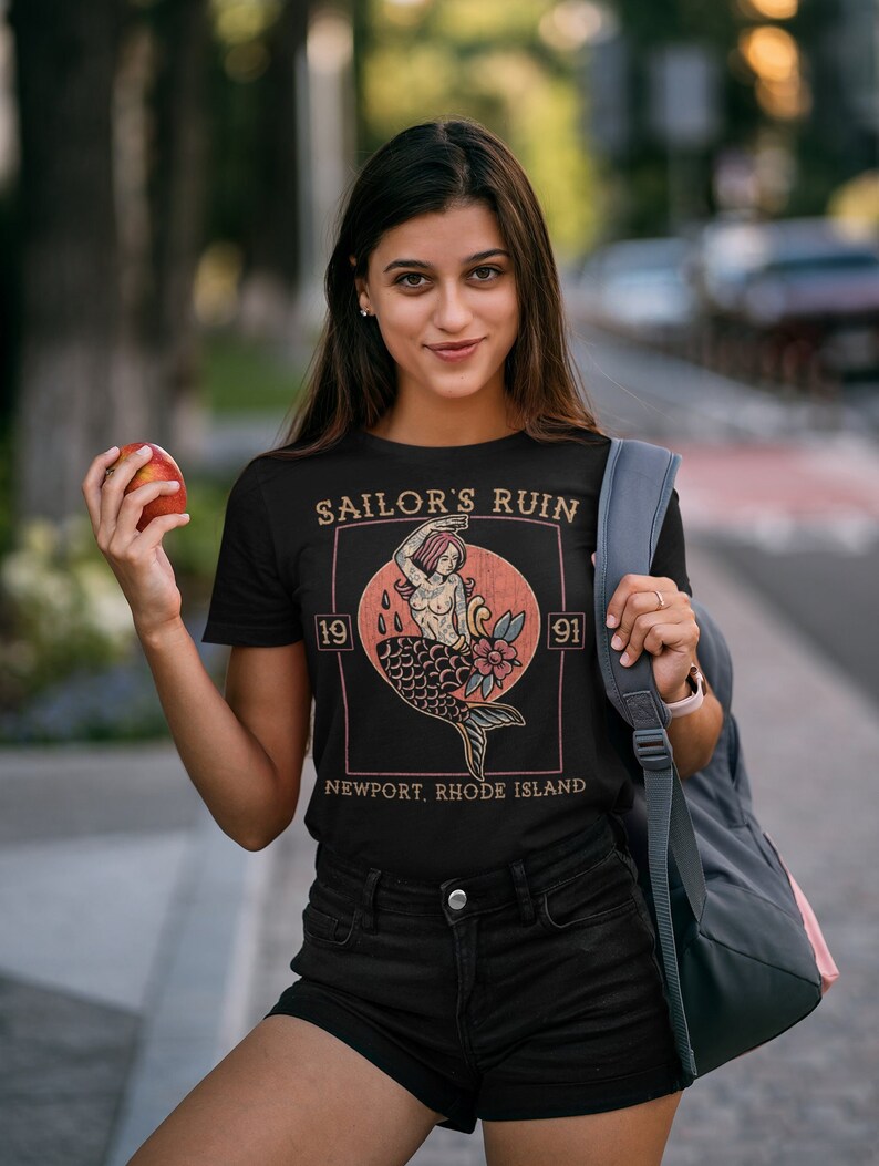 May include: Black t-shirt with a vintage-style graphic of a mermaid with the text "Sailor's Ruin 1991 Newport, Rhode Island".