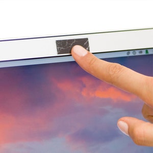 May include: A laptop computer with a black privacy cover over the webcam. A finger is shown covering the webcam cover.