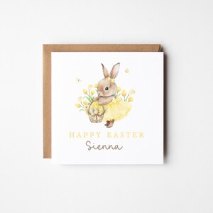 May include: A square Easter greeting card with a watercolor illustration of a bunny wearing a yellow tutu and holding a basket of eggs. The card reads "Happy Easter Sienna" in yellow and gray text, set against a white background.