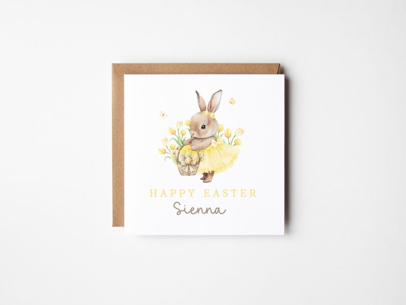 May include: A square Easter greeting card with a watercolor illustration of a bunny wearing a yellow tutu and holding a basket of eggs. The card reads "Happy Easter Sienna" in yellow and gray text, set against a white background.