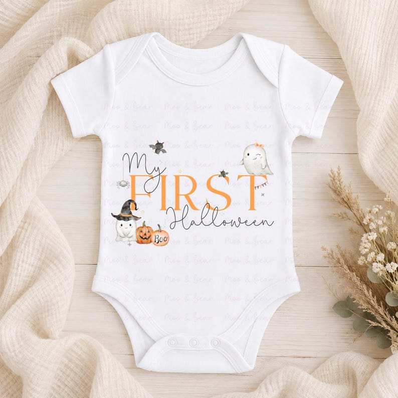May include: A white short-sleeve baby bodysuit featuring a graphic print with the text My FIRST Halloween in orange and black. The design includes illustrations of two ghosts, one wearing a witch hat, a spider, a bat, and two orange pumpkins.