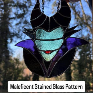 May include: Stained glass art piece featuring the character Maleficent. The artwork showcases a black horned head, a purple collar, and a teal face with a red mouth. The text "Maleficent Stained Glass Pattern" is at the bottom.