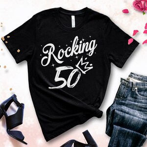 May include: Black t-shirt with white text that says "Rocking 50" with a crown above the zero. The number 50 is written in a brushstroke style.