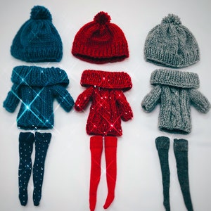Pode incluir: Três conjuntos de roupas de boneca, cada um com um chapéu de malha, um suéter e meias a condizer. Os conjuntos são em verde-azulado, vermelho e cinza. O conjunto verde-azulado tem bolinhas brancas nas meias. O conjunto vermelho tem meias vermelhas. O conjunto cinza tem meias cinzentas.