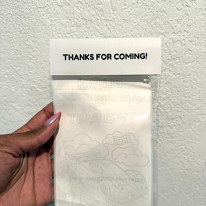 May include: A clear cellophane bag with a white card attached. The card reads "THANKS FOR COMING!" in black text. Inside the bag is a coloring sheet with a race car design and the text "TWO FAST 21".