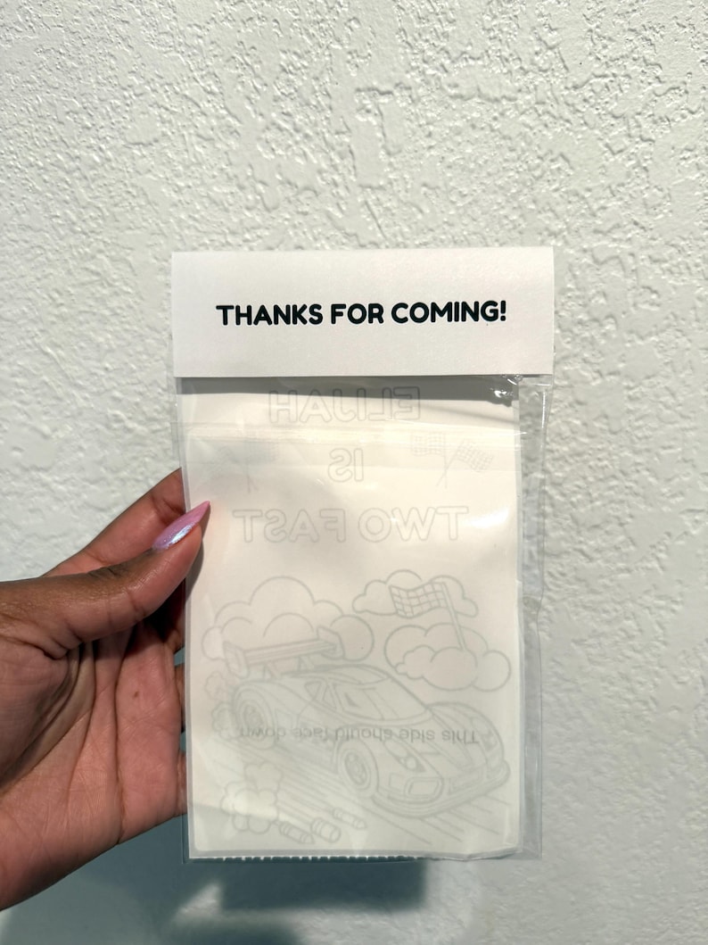 May include: A clear cellophane bag with a white card attached. The card reads "THANKS FOR COMING!" in black text. Inside the bag is a coloring sheet with a race car design and the text "TWO FAST 21".