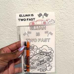 May include: A clear plastic bag containing a coloring page and two crayons. The coloring page features a race car and the text "ELIJAH IS TWO FAST." The crayons are black and orange.