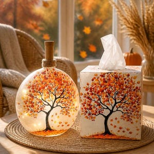 May include: A round glass bottle with a cork stopper and internal lights, paired with a square tissue box. Both items feature a painted autumn tree design with orange, yellow, and red leaves against a white background, creating a cohesive set.