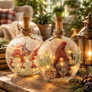 May include: Two round glass bottles with cork stoppers, each wrapped with twine at the neck. The bottles feature internal fairy lights and illustrations of gnomes in winter settings with pine trees and lanterns, creating a glowing effect.