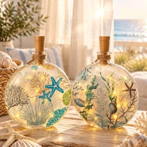 May include: Two round glass bottles with cork stoppers, each filled with internal string lights and decorated with colorful illustrations of seashells, starfish, and coral reefs in shades of blue, green, and brown, creating a coastal display.