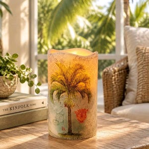 May include: A cylindrical LED candle featuring a palm tree illustration, a red crest, and the letter B. The surface has a textured, vintage-style pattern with script text. The candle emits a warm, soft glow from the top, creating a light effect.