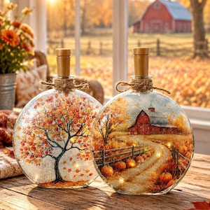 May include: Two round glass bottles with cork stoppers and twine bows. One bottle features a painted autumn tree with orange and yellow leaves. The other bottle displays a painted rural scene with a red barn, a dirt path, and orange pumpkins.