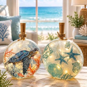 May include: Two round glass bottles with cork stoppers and internal string lights. One bottle features a blue sea turtle and orange coral reef design. The other bottle displays blue starfish, seashells, and green coral illustrations.