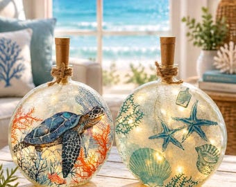 May include: Two round glass bottles with cork stoppers and internal string lights. One bottle features a blue sea turtle and orange coral reef design. The other bottle displays blue starfish, seashells, and green coral illustrations.