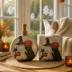 May include: A round decorative bottle and a square tissue box holder, both featuring a printed illustration of a ghost wearing a witch hat, a black cat, and a pumpkin. The items have a distressed off-white finish and are placed on a round mat.