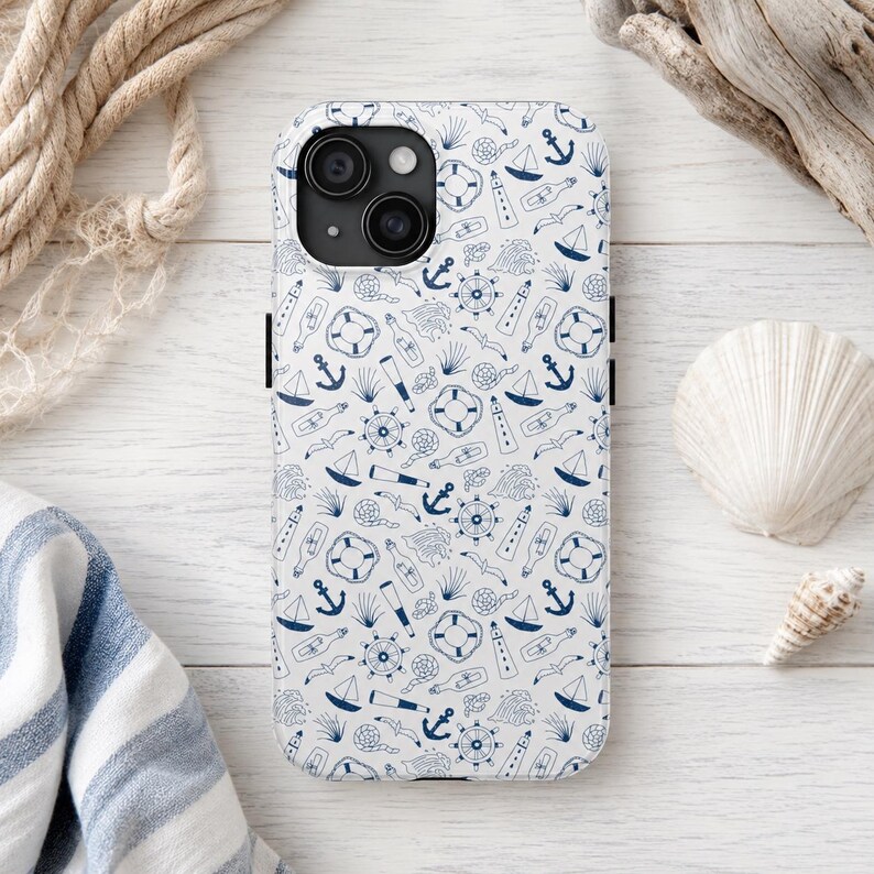 Puede incluir: Una funda de tel&eacute;fono blanca con un patr&oacute;n n&aacute;utico azul marino que presenta anclas, veleros, salvavidas y otros elementos mar&iacute;timos. La funda tiene un m&oacute;dulo de c&aacute;mara negro.