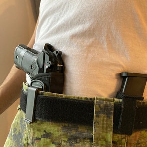 May include: A black handgun with a black holster attached to a black belt with a camouflage pattern. The holster is secured to the belt with a black clip.