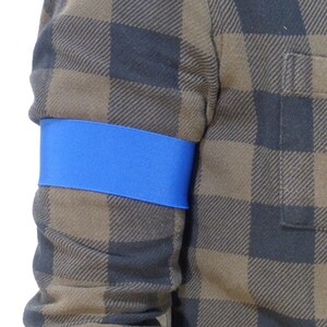 Pode incluir: Uma pessoa vestindo uma camisa xadrez marrom e preta com uma faixa azul no braço esquerdo.