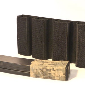 May include: A black tactical magazine pouch with four slots for magazines. The pouch has a hook and loop closure and is made of durable nylon. A black magazine with a camouflage wrap is in front of the pouch.