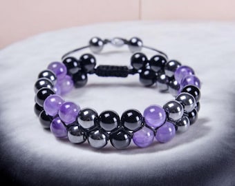 May include: A double-strand bracelet featuring alternating amethyst and black hematite beads. The bracelet is secured with a black cord and a sliding knot.