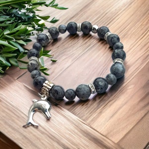 Puede incluir: Un brazalete de piedras preciosas azul oscuro con detalles plateados y un dije de delf&iacute;n plateado.