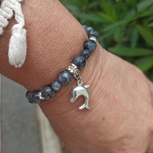 Puede incluir: Un brazalete de piedras grises con un dije de delf&iacute;n plateado. El brazalete est&aacute; hecho de cuentas redondas y tiene un cierre plateado.