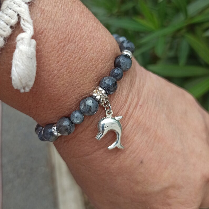 Puede incluir: Un brazalete de piedras grises con un dije de delf&iacute;n plateado. El brazalete est&aacute; hecho de cuentas redondas y tiene un cierre plateado.
