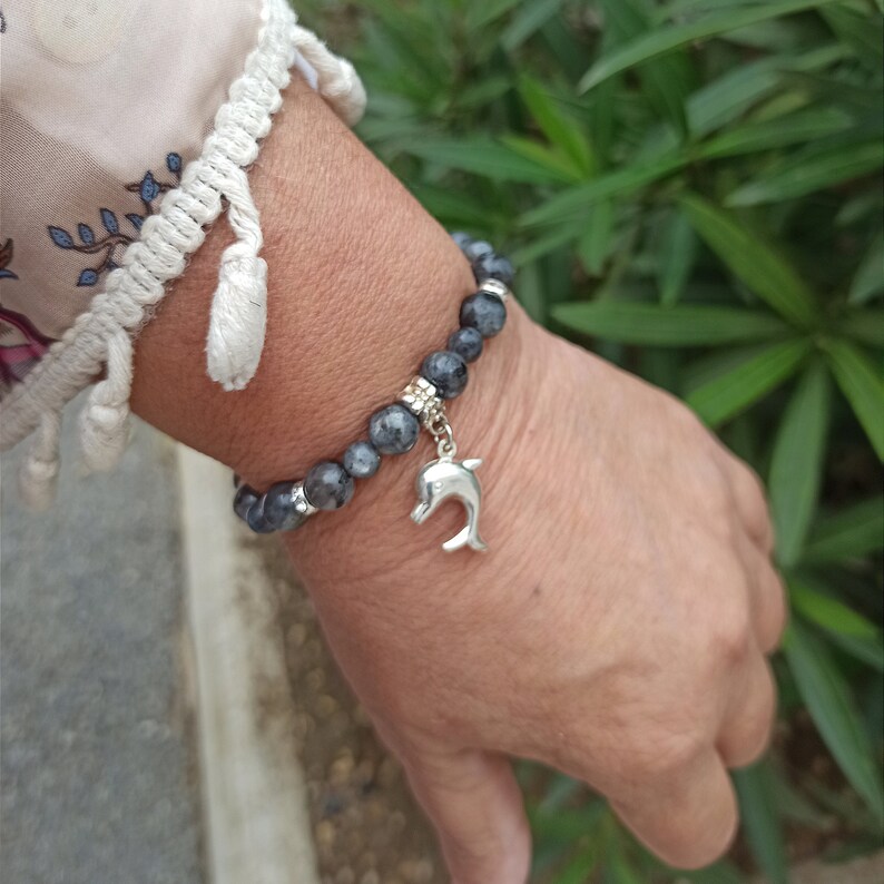 Puede incluir: Un brazalete de cuentas grises con un dije de delf&iacute;n plateado. El brazalete est&aacute; en la mu&ntilde;eca.