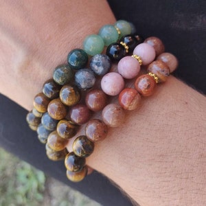 Può includere: Una collezione di braccialetti di perline in vari colori, tra cui verde, nero, rosa e marrone. I braccialetti sono fatti di perline rotonde e sono impilati l'uno sull'altro. Le perline hanno una finitura lucida e sono infilate su elastico.