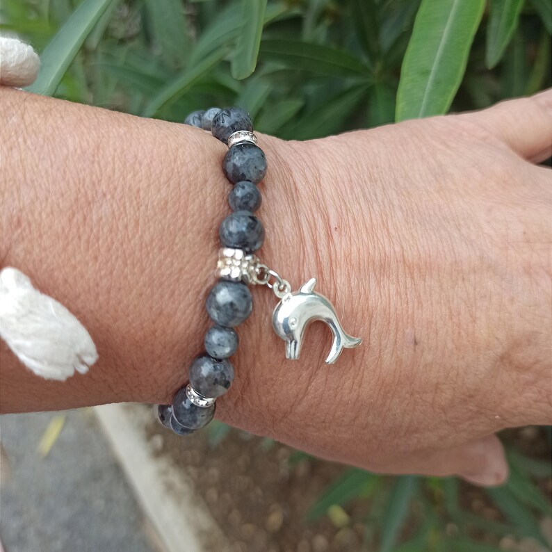 Puede incluir: Un brazalete de cuentas grises con un dije de delf&iacute;n plateado. El brazalete est&aacute; en la mu&ntilde;eca.