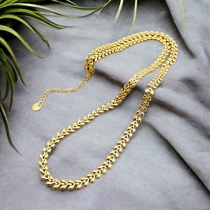 Peut inclure: Un collier en chaîne dorée avec un design délicat en forme de feuille. La chaîne est composée de petits maillons interconnectés qui créent un aspect fluide et élégant.