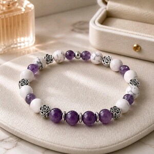 Peut inclure: Un bracelet de perles composé d'une alternance de perles blanches à motifs marbrés, de perles d'améthyste violettes translucides et de petites entretoises en métal argenté en forme de fleurs, le tout monté sur un cordon élastique circulaire.