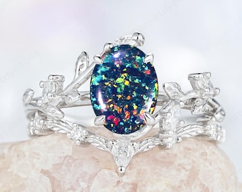 May include: A silver ring with an oval, dark blue opal gemstone. The ring features a floral design with small white gemstones and delicate leaf accents. The opal has a colorful, iridescent appearance.