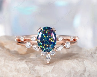 Könnte beinhalten: Ein Verlobungsring aus Roségold mit einem ovalen Opal-Edelstein, der von kleineren Diamanten umgeben ist. Der Ring hat ein zartes, florales Design mit einem Band, das mit kleineren Diamanten verziert ist.