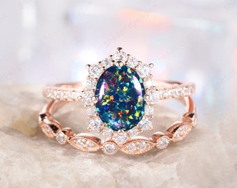 Könnte beinhalten: Ein Verlobungsring aus Roségold mit einem großen ovalen Opal als Mittelstück, umgeben von einem Heiligenschein aus kleineren Diamanten. Der Ring liegt auf einem weißen Hintergrund.