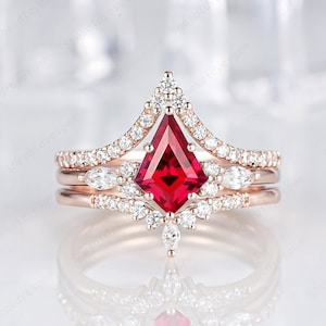 May include: A three-piece rose gold engagement ring set with a large, red, square-shaped gemstone surrounded by smaller, clear gemstones. The ring is set on a white background.
