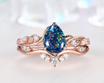 Könnte beinhalten: Ein Verlobungsring aus Roségold mit einem birnenförmigen Opal, einem filigranen Blattdesign und kleinen Diamanten. Der Opal ist in einem leuchtenden Blau-Grün mit roten und orangen Schimmern.
