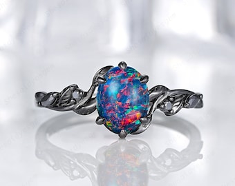 May include: Black opal engagement ring with a delicate floral design. The ring features a large oval-shaped opal with a vibrant blue, green, and red color. The band is black and has small black diamonds on either side of the opal.