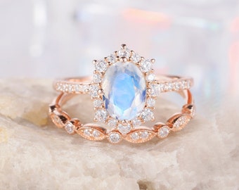 May include: A rose gold engagement ring set with a large oval moonstone surrounded by smaller diamonds. The ring is set on a white background.