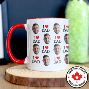 May include: White ceramic mug with a red rim and handle. The mug is covered in a pattern of repeated images of a man's face with the text "I ♥ DAD" printed below each face.