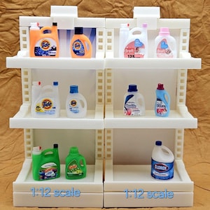 May include: A display of miniature laundry detergent bottles, including brands like Tide, Dreft, Gain, and Clorox, arranged on white shelves. The bottles come in various colors and sizes, with labels visible. The text "1:12 scale" is at the bottom.