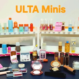 May include: A collection of various beauty products including skincare bottles, makeup compacts, and tubes arranged on two white tiered shelves and a dark surface. The text ULTA Minis is displayed in orange at the top of the image.