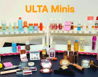 May include: A collection of various beauty products including skincare bottles, makeup compacts, and tubes arranged on two white tiered shelves and a dark surface. The text ULTA Minis is displayed in orange at the top of the image.