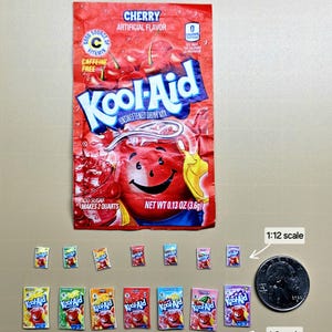 May include: A close-up of a miniature cherry-flavored Kool-Aid packet, along with several other miniature packets in various flavors. The packets are arranged in two rows, with the cherry packet in the center of the bottom row. The packets are all about 1/2 inch tall. The image also includes a U.S. quarter for scale.