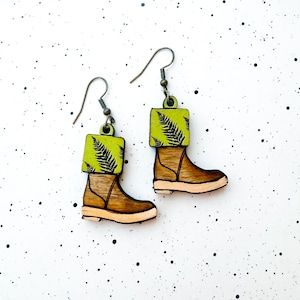 May include: A pair of wooden earrings shaped like boots with a green fern pattern on the top of the boot.