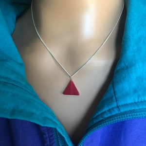 May include: A silver chain necklace with a red triangular pendant.