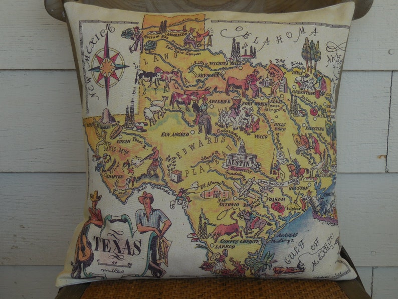 May include: A decorative pillow featuring a vintage-style map of Texas with illustrations of landmarks and animals. The map is surrounded by a beige border and the text "Texas" is written in a stylized font at the bottom.