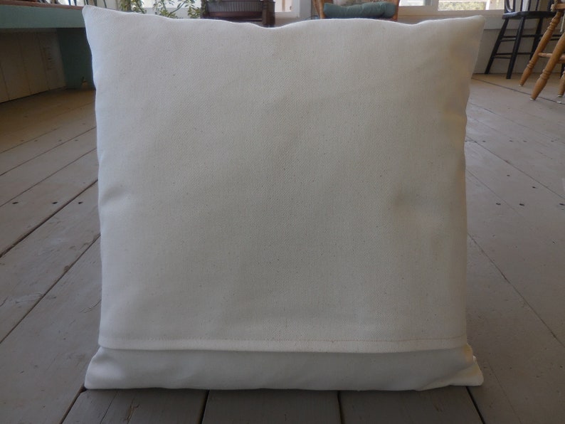 May include: A plain white pillow with a white fabric backing. The pillow is lying flat on a wooden floor.