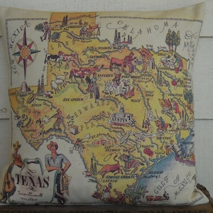 May include: A vintage-style map of Texas on a beige pillow. The map is yellow and features illustrations of various landmarks, animals, and cities. The text "Texas" is written in a large font at the bottom of the map, along with the words "700 miles".